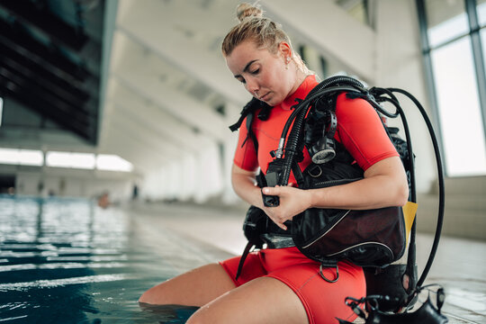 Woman diver preparing diving equipment at swimming pool, adjusting safety gear before scuba training