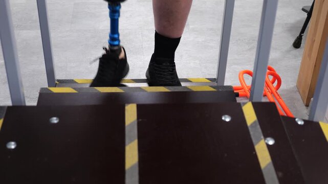 Disabled man with prosthetic leg walking down stairs during physiotherapy