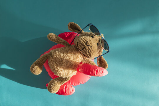 Knitted Plush Sheep in Sunglasses on Pink Pool Flamingo Float Against Blue Water.