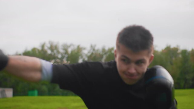 outdoor boxing session with two men in grassy park, intense power drill with close range punches, mitt work and coach cues, heavy strikes and reactive defense under overcast sky, gritty training