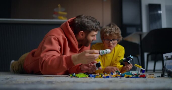 Father and young son lying on the living room floor building colorful toy brick creations together during a cozy indoor family playtime