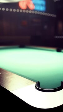 A green pool table is seen with balls scattered on its surface. The setting is a bar with low lighting and a vibrant atmosphere. People may be playing or watching games.