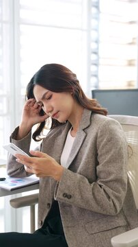 Upset  , Serious young asian businesswoman using mobile phone in office looking frustrated at mobile phone screen, holding head. chatting online, texting message.