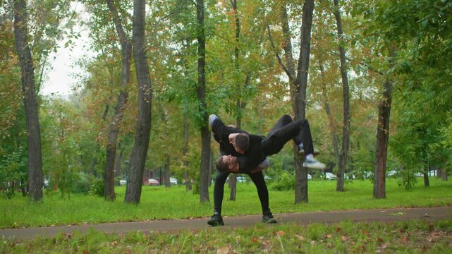 park altercation between two men, casual sparring escalates into struggle, one man trips on path then receives hand up, tension dissolves into brief apology, autumn trees frame peaceful scene