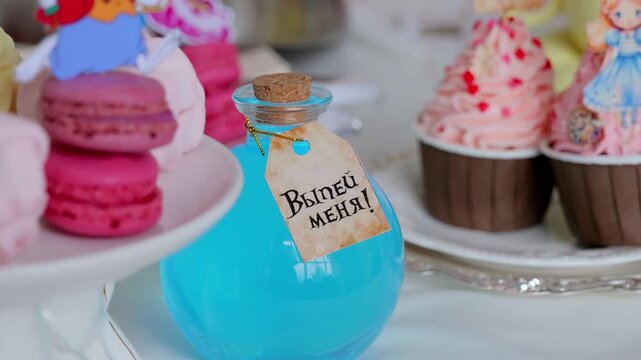 Closeup Blue Vial Near Pink Cupcakes And Macarons, Turquoise Elixir With Cork Playful Topper And Glossy Plate, Styled By Event Planner, Celebration Mood, Bright Studio, Translation: Drink Me