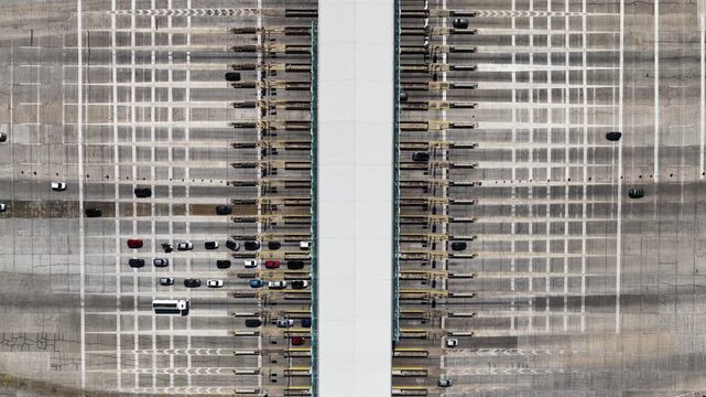 High angle top down view of cars and other vehicles passing through the toll booths of a busy highway, showcasing the constant flow of traffic on a major transportation route