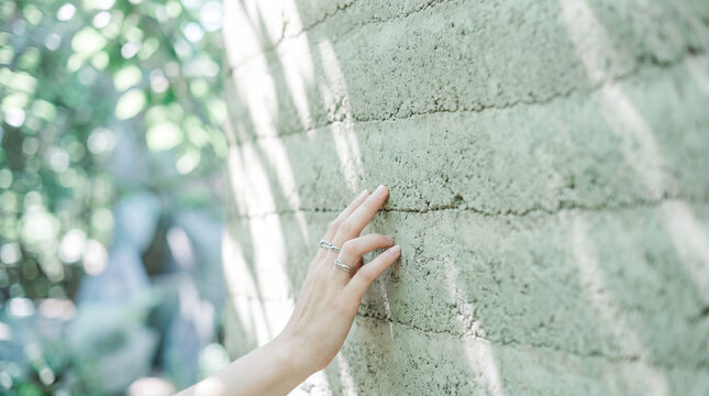 Person touching textured rammed earth architectural wall in soft light