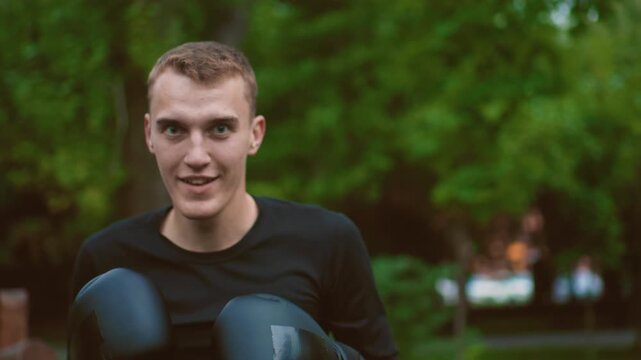 young boxer training in park wearing gloves, closeup shots capture focused expressions, light sweat, green trees background, punching motion and later relaxed smile, athletic black training shirt,
