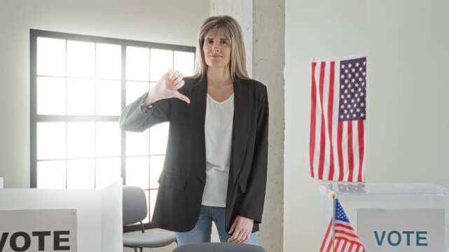Woman thumb down gesture toward ballot box and vote sign in building polling place with american flag visible; dissent concern.