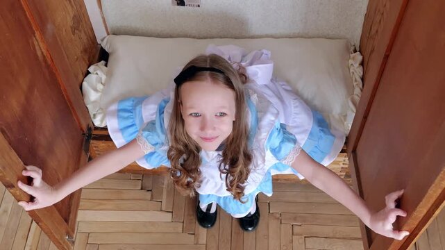 Curious Girl Peeks Upward. Child Peeking From Vintage Wardrobe With Inquisitive Expression. Young Caucasian Girl Glances Upward From Charming Hideaway With Rustic Flooring And Old Doors