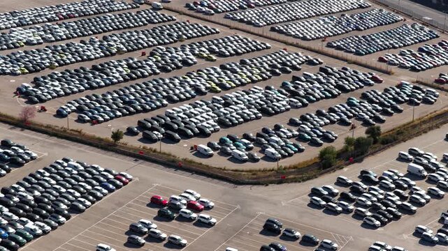 Aerial drone footage revealing thousands of new cars parked in perfect rows at a large industrial lot, highlighting the scale of modern automotive manufacturing and global distribution