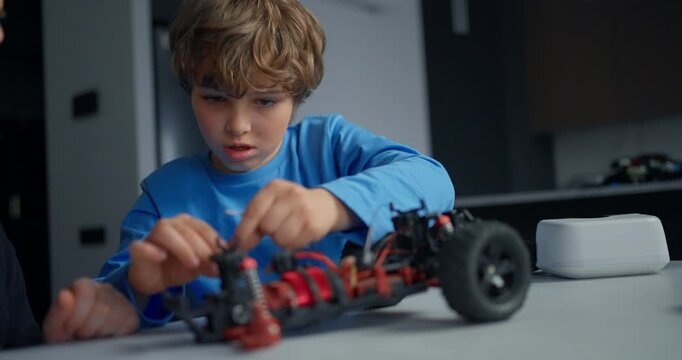 Young boy concentrating as he assembles a small remote control toy car on a table indoors, exploring mechanics, electronics, and hands-on STEM learning