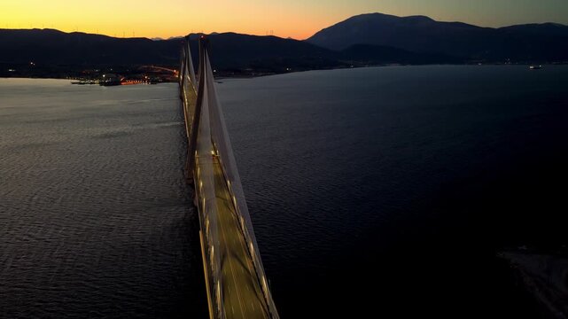Magnificent aerial view of the illuminated rio-antirrio bridge in greece, connecting the peloponnese to the mainland with car traffic flowing across the calm waters of the gulf of corinth at dusk