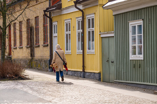 Elderly woman walking along quiet cobblestone street with traditional wooden houses in Scandinavian town.