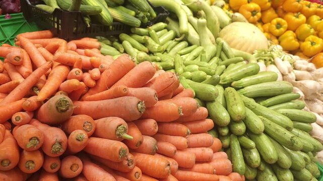 Colorful display of fresh vegetables at a local market, featuring piles of carrots, zucchini, bell peppers, and ginger arranged in neat rows. Close-up shot highlighting natural textures, vibrant color
