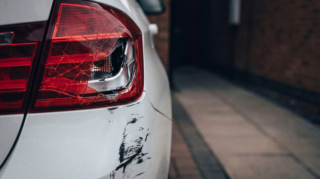 Broken taillight on white car after collision. Damage on vehicle bumper following road accident. Insurance claim concept for repair service, transport safety and traffic incident analysis.