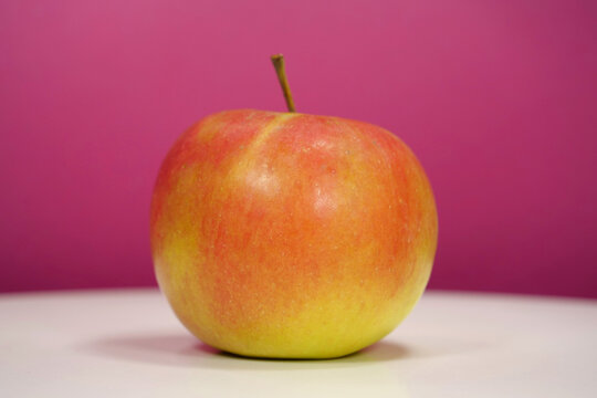 Ripe red yellow fresh apple on pink background, close-up