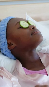 Vertical video: Relaxing girl in pink robe reclining on bed, cucumber slices bringing calm
