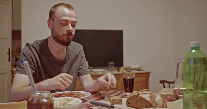 A man savors his meal alone at a dining table, eating food and bread while sipping a drink. This scene captures a moment of quiet, everyday life and personal routine in a comfortable home environment.