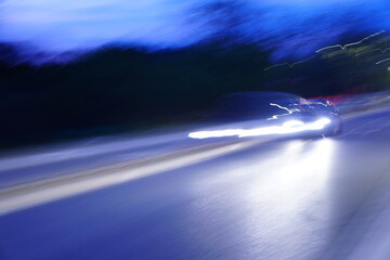 A long exposure evening shot featuring motion blur and vibrant light trails from car headlights, creating glowing, fluid lines against the dark background. © Lena