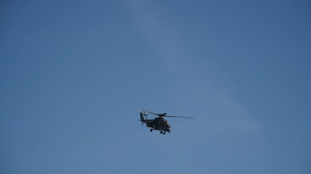 Silhouette of military helicopter flying against blue sky and making turn. Bank of combat helicopter on mission near airfield during patrolling. Ensuring security during peacekeeping mission.