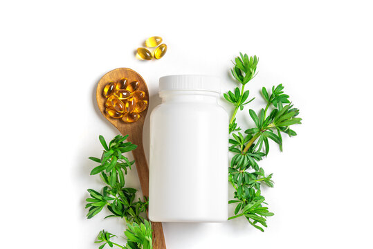 White blank bottle with natural herbal supplements or plant based oil softgels and green leaves
