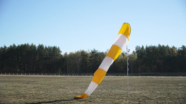 Windsock in form of striped fabric tube on pole weakly flapping in wind near airport runway. Indication of flying weather with light wind on sunny day.