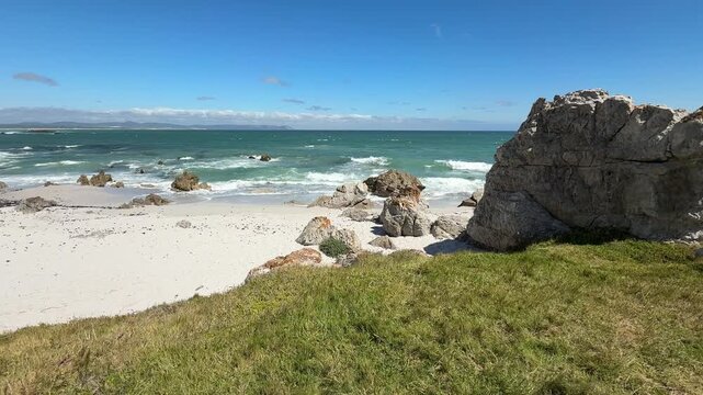 Hermanus coastline in South Africa with ocean waves, sandy beach and deep blue sky, beautiful summer landscape with relaxed holiday atmosphere.