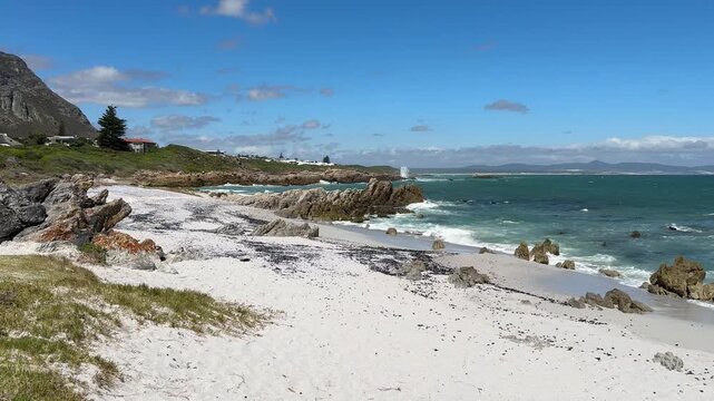 Hermanus coastline in South Africa with ocean waves, sandy beach and deep blue sky, beautiful summer landscape with relaxed holiday atmosphere.