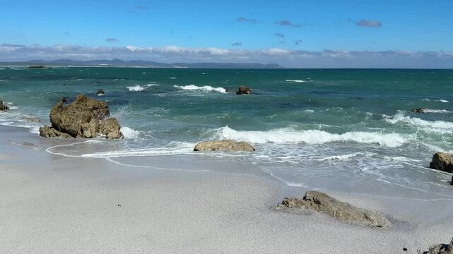 Hermanus coastline in South Africa with ocean waves, sandy beach and deep blue sky, beautiful summer landscape with relaxed holiday atmosphere.