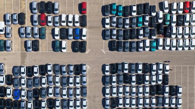 Aerial top-down perspective showing countless new cars neatly parked in a large distribution lot, highlighting the scale of automotive manufacturing, logistics, and global supply chain operations