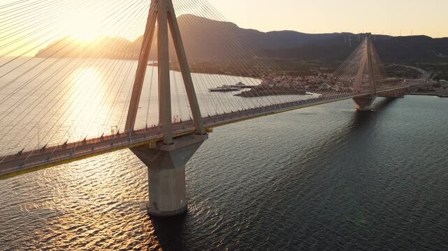 Epic pull-back drone shot revealing a monumental cable-stayed bridge at sunset, showcasing transportation flow with trucks and buses crossing the water.
