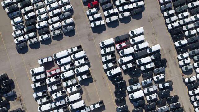 Aerial top-down view of a massive car park filled with brand new vehicles awaiting sale or export, showcasing the scale of the automotive industry and global logistics