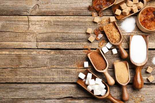Different types of sugar in scoops on wooden table, flat lay. Space for text