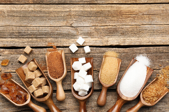 Different types of sugar in scoops on wooden table, flat lay. Space for text