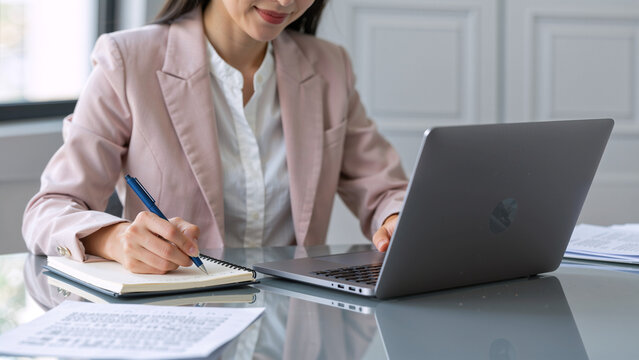 Woman working on laptop and writing in notebook