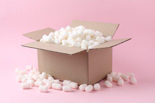 Cardboard box with styrofoam pieces and gift on pink background