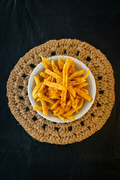 Flat lay de porci&oacute;n de papas fritas picantes en taz&oacute;n blanco. El encuadre amplio muestra el contraste del mantel de yute con el fondo negro.