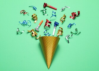 Naklejka premium Shiny party streamers, horns and cone on green background, flat lay
