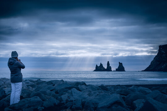 Rear view of a young Woman in warm clothing on a stormy day standing on a rocky beach looking out to sea, Iceland