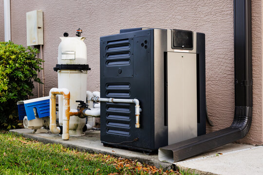 Modern natural gas swimming pool heater unit and pool water filtration equipment on concrete slab outside of house.