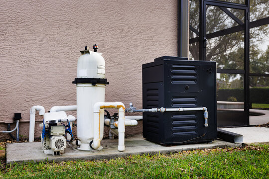 Modern natural gas swimming pool heater unit and pool water filtration equipment on concrete slab outside of house.