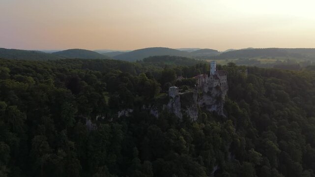 Schloss Lichtenstein in der Abendsonne, aufgenommen mit Drohne. Das 19. Jahrhundert-Schloss thront spektakulaer ueber dem Albtrauf nahe Reutlingen, Deutschland mit Blick auf Wald und Tal. 