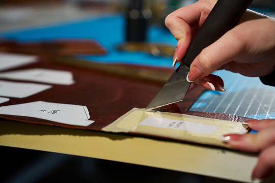 Artisan is slicing through a raw cowhide along a paper template with a leatherworking blade.