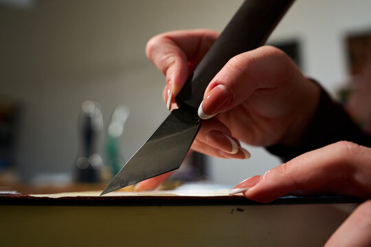 Artisan slicing through raw cowhide with a professional leatherworking blade close up.