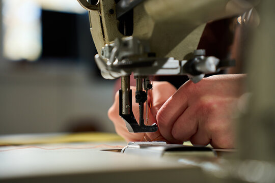 Artisan hands threading a heavy-duty industrial sewing machine in a workshop.