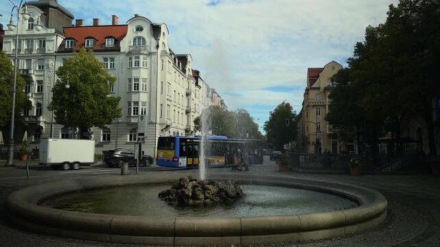 The historic Prinzregent-Luitpold-Brunnen fountain stands proudly at Prinzregentenplatz in Munich, Germany, as buses and traffic move past on a sunny autumn day in this vibrant city square.