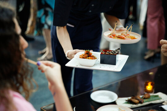Elegant catering scene at a stylish cocktail event where a waiter serves a seafood platter to guests. People are taking food directly from the tray, capturing a refined social moment of sharing,