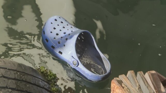 Single plastic clog floating in polluted water near shore, environmental problem concept showing plastic waste contamination and marine pollution in natural environment
