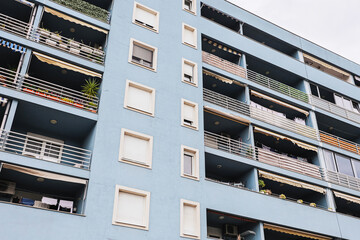 Blue apartment block facade with balconies and shuttered windows. Everyday urban living appears in plants and laundry. Residential architecture forms a modern city background with local character. © Paweł Michałowski